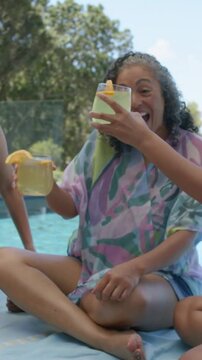 Vertical video: Reaching woman in wrap taking two drinks to toast at pool, with sippy lid from pal