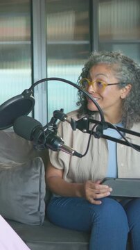 Vertical video: Holding cup after prompt, woman with glasses in pod reading tablet, talking to mic