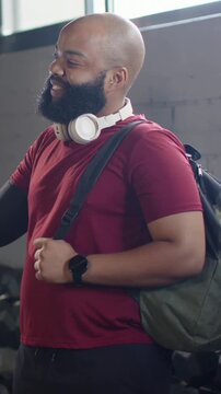 Vertical video: Reaching as arm shows, man in red tee bumping fists  and  fixing strap in gym, greet