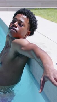 Vertical video: Leaning shirtless man turning head to face camera as camera reframes at pool coping