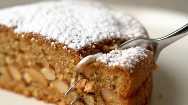 Close-up of a delicious slice of nut cake with powdered sugar and a fork.
