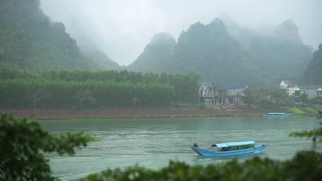 Morning Boat Traverses Lush Banks. Asian Commuters Cross Phong Nha In Tranquil Boat Ride. Sunrise Casts Misty Atmosphere Over Ferry Navigating Vibrant Green Riverbanks In Phong Nha