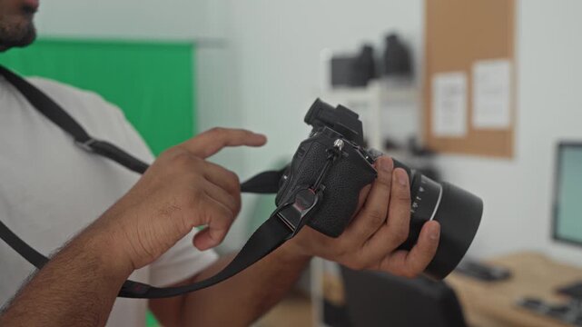 Man holding mirrorless camera with lens and pointing finger to dial against green backdrop in studio; concentration skill craft.