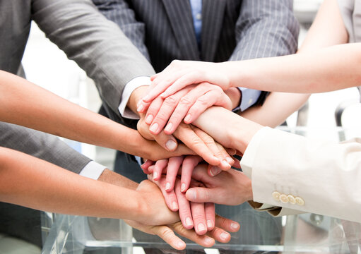 Diverse business professionals stacking hands together in unity, symbolizing teamwork, collaboration, and successful partnership in corporate environment.
