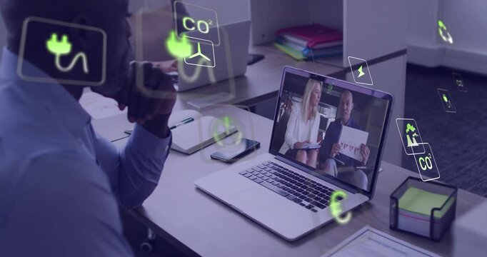 Businessman watching laptop, remote presenters sharing data showing energy icons across desk screen