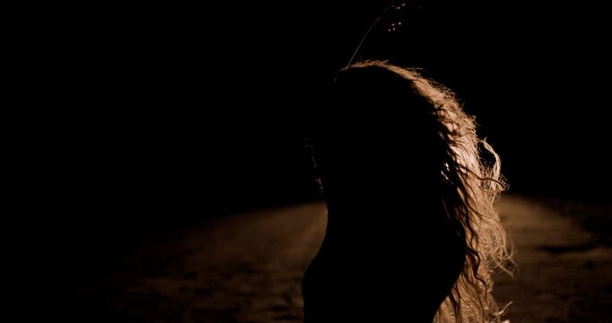 Girl dances in silhouette under car headlights in a dark setting at night