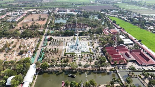 High-quality cinematic drone footage of a smooth diagonal descent towards the stunning white pagoda at Wat Phai Rong Wua temple in Suphan Buri province, Thailand.