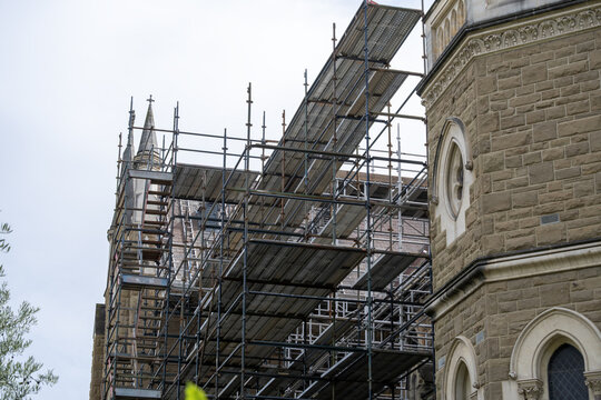 Scaffolding installed around a historic stone church in Melbourne, Australia, indicating restoration and maintenance work. Heritage religious architecture under renovation, preservation, conservation