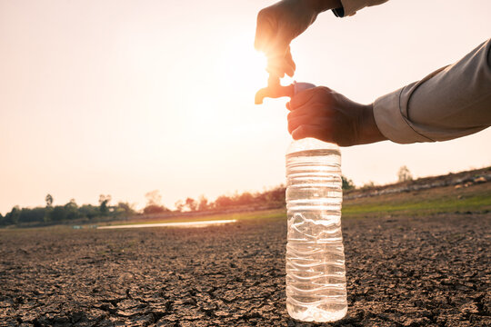 Water scarcity concept, Filling plastic bottle from faucet in dry cracked land at sunset.