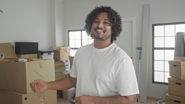 Man in white t shirt folds arms beside packed moving boxes in new home building; moving day quiet pride.