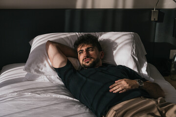 Fototapeta premium Young man lying in bed relaxing during morning sunlight, contemplating and thinking about his life goals. Lifestyle and wellness concept