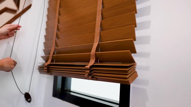 Hands Pulling Cord to Lower Wooden Venetian Blinds Over Window