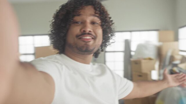 Man with outstretched arm taking selfie and presenting packed boxes and ladder in new home building; moving joy.