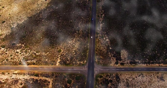 Showing four-way paved intersection crossing arid scrubland with grid markers and light vehicle