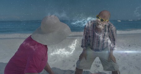 Fototapeta premium Leaning senior couple smiling at beach, wearing pink top, sunhat, plaid shirt, nebula overlay