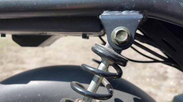 Motorcycle suspension spring and rear shock absorber close-up in outdoor setting under bright daylight in rural environment.