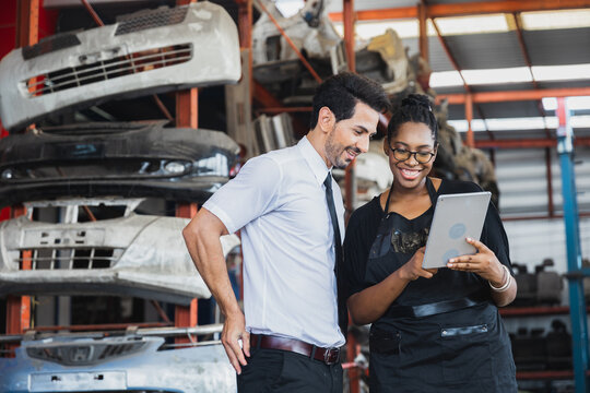 Diverse business partners using tablet to check auto parts in industrial warehouse storage