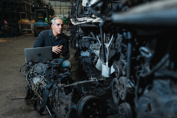 Fototapeta premium Supervisor with laptop inspecting used car engines in automotive spare parts warehouse