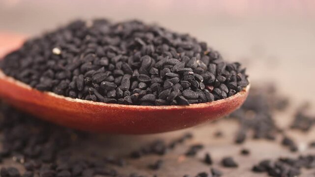 Black cumin seed is shown in a wooden spoon on a table