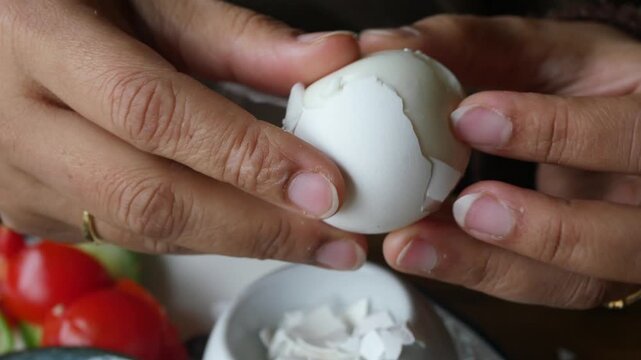 A person is peeling a hard-boiled egg in a kitchen while getting ready to cook