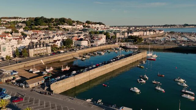 St Peter Port Harbour Guernsey drone flight over Victoria Marina Crown Pier and careening hard in late afternoon sun with backdrop of the town and Belle Greve Bay in the distance