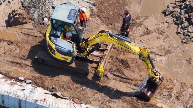 Overhead View of Yellow Mini Excavator Digging in Muddy Construction Site