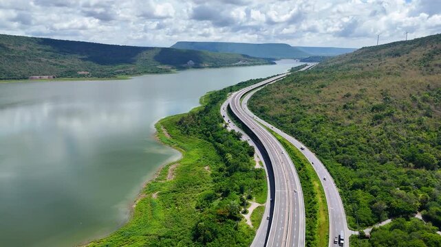 Aerial view of highway running along river and green hills. Transportation, infrastructure, travel and logistics concept