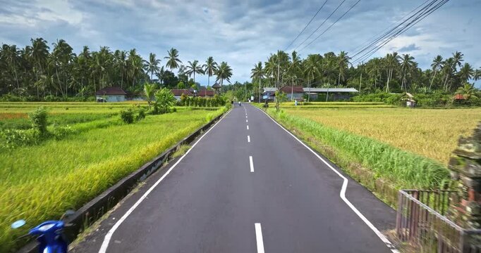 Iconic Candi Bentar gate standing on the tropical road entering a rural village with lush green rice fields and palm trees under a cloudy sky. Travel and explore Bali, Indonesia. Drone flight footage