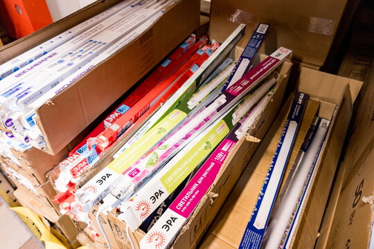 Various brands of light tubes arranged in cardboard boxes in a storage area for electrical supplies in a warehouse environment