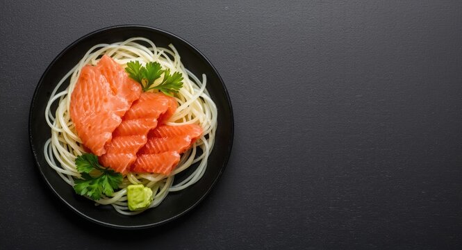 Top view of raw salmon sashimi set with funchosa noodles parsley and wasabi on dark surface with copy space