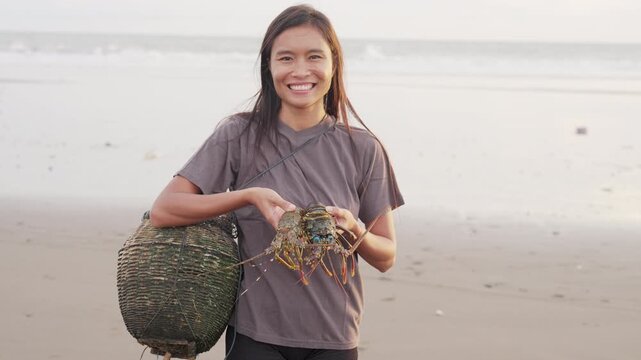 Portrait, smiling southeast asian woman fisherman with spiny lobsters on beach, sea in background