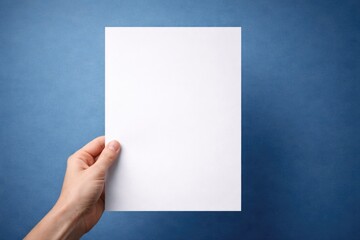 Obraz premium A hand holding a blank A4 sheet against a smooth blue textured background with copy space for text