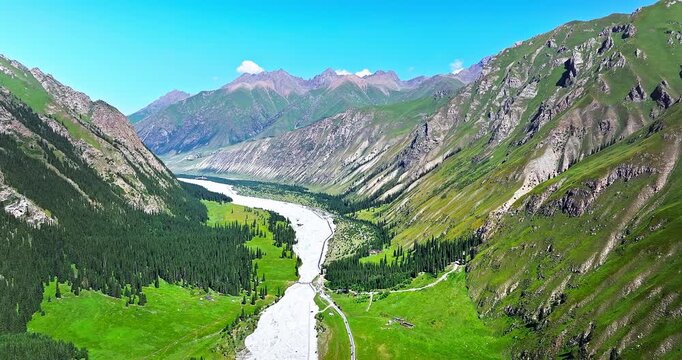 Aerial view of a lush green valley with a meandering river and dense forest in the Tianshan Mountains, Xinjiang, China.