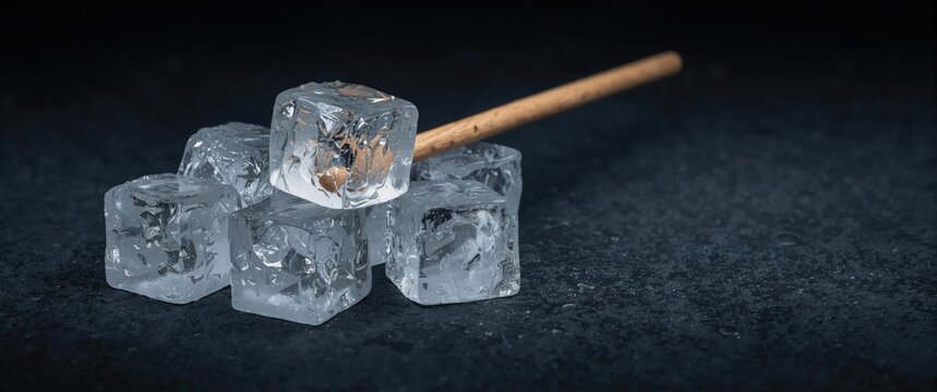 Close view of ice cubes with a wooden ice pick on a textured deep dark backdrop focusing on ice clarity and texture