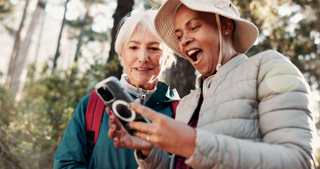 Fototapeta premium Hiking, excited and senior women with phone for wellness, fresh air and online app for navigation. Friends, shock and elderly people on smartphone for direction, trekking and exercise on nature trail