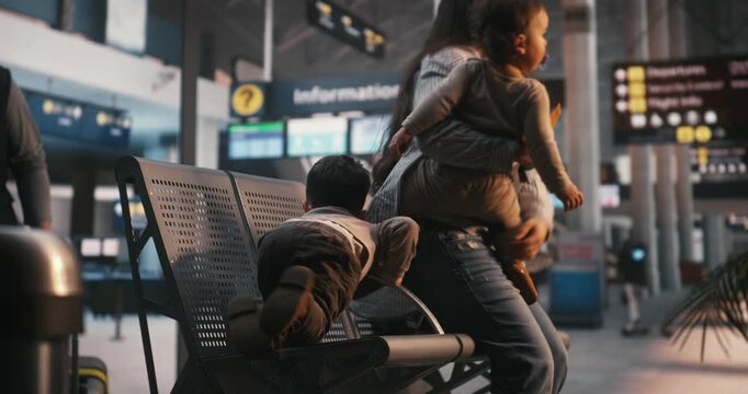Mother and Two Small Kids Sit on Terminal Benches, Interacting With Smartphones and Passports. Reality of Traveling With Toddlers, Passenger Waiting Experience, Lifestyle of Modern Family Vacations.