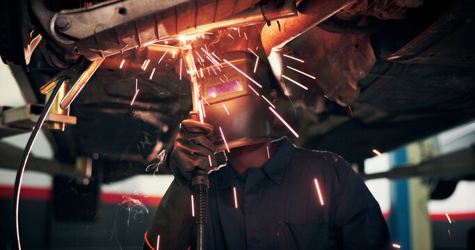 Mechanic, welding and person with tools by car for diagnostics, maintenance or auto service. Workshop, sparks and technician with equipment for vehicle inspection, fixing or engine repair with helmet