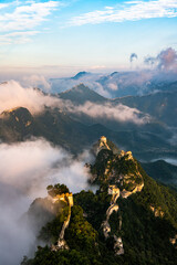 Fototapeta premium Aerial view of the Jiankou section of the Great Wall of China emerging through clouds at sunrise. The ancient wall winds along steep mountain ridges, partially covered by drifting mist