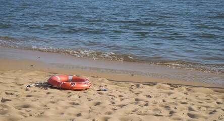 Obraz premium Lifebuoy lying on smooth sand near calm coastal waterline