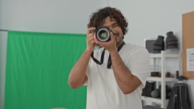 Man photographer holding camera to eye in studio with green screen, hands on lens and shutter; concentration craft.