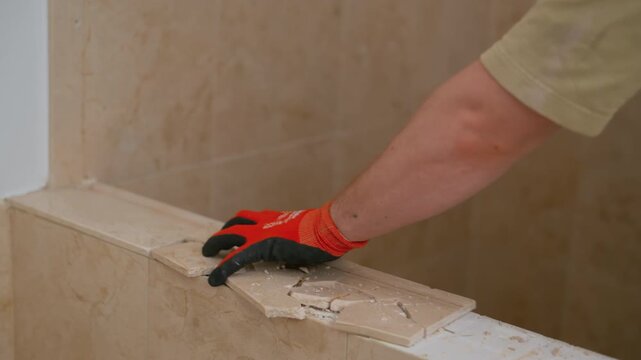 worker using a hammer to remove ceramic tiles from a bathroom wall during renovation. Demolition phase showing breaking tiles and surface preparation for new installation .