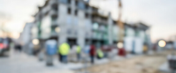 Obraz premium A blurred view of a construction site with workers engaged in various tasks. The scene includes building structures and construction equipment in the background.