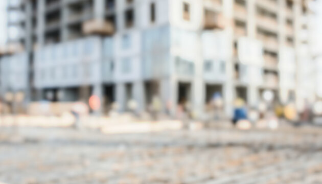 A blurred image of a construction site with workers engaged in various tasks on a building project. The background shows incomplete structures.