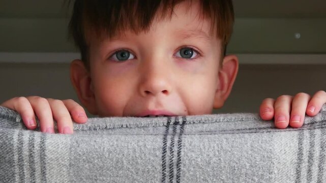 A funny cheerful boy peeks out from behind a plaid screen