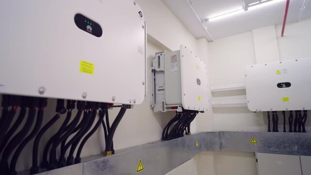 Multiple solar inverter units with electrical cables mounted on wall inside industrial power control room