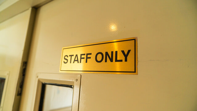 a close-up photograph of a metallic gold-colored sign that reads staff only, mounted on a clean cream door to indicate restricted access for authorized personnel within a professional building.