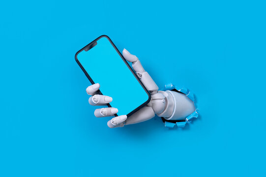 Robot hand holding a smartphone through a torn blue paper background concept