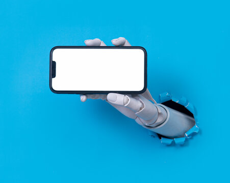Robot hand holding a smartphone through a torn blue paper background concept