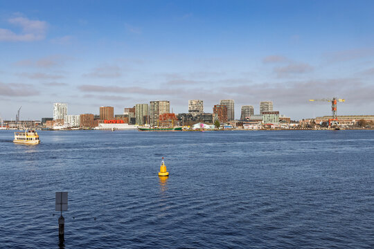 View across the IJ river towards the Amsterdam Noord skyline featuring the Botel, modern apartment buildings, and industrial cranes in the sun.  Amsterdam Netherlands, 28 december 2025