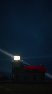 Vertical Screen: Lighthouse glowing in mist with sweeping light beam across night sky near Mendocino, California, USA forming dramatic coastal cinematic scene